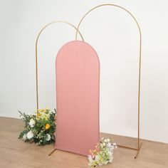 a pink and gold arch with flowers on the floor in front of it, against a white wall