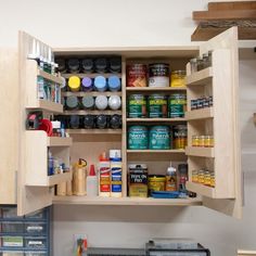 an open cabinet in a kitchen filled with lots of paint and other things on the shelves