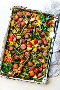 a sheet pan filled with sausage and veggies on top of a white table