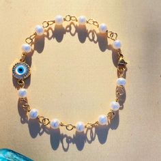 Our beautiful Evil Eye and Pearl Bracelet is crafted with 14Kt gold filled wire and clasp and features Mother of Pearl and Zirconia Evil Eye charm. Handmade with LOVE in the USA, this protective bracelet holds thousands of years of history. The iconic symbol of the evil eye (🧿) found in Latin America and parts of Asia is traditionally believed to ward off negative energy. Shine bright with this meaningful piece! Evil Eye Pearl Bracelet, Elegant Gold-plated Evil Eye Bracelet Gift, Adjustable Metal Evil Eye Bracelet, Blue Evil Eye Metal Bracelet, Turkish Glass Evil Eye Bracelet Gold Metal, Evil Eye Charm, Jewelry Lookbook, Cuff Bangles, Latin America