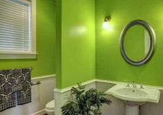 a bathroom with green walls and white fixtures, including a round mirror above the sink