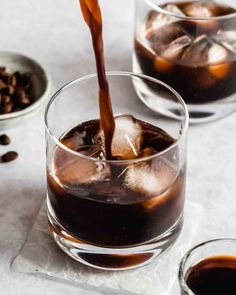 two glasses filled with ice and coffee being poured into one glass, on top of the other