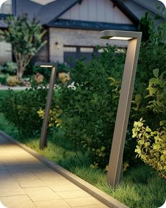 three lights are lit up on the side of a sidewalk in front of some bushes