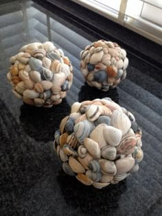 three seashell balls sitting on top of a black table next to a glass window