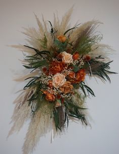 an arrangement of flowers and feathers is hanging on the wall