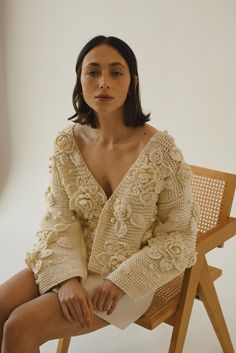 a woman is sitting on a chair with her legs crossed and wearing a white sweater