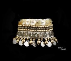 A handmade New Guinea white braided rope wide bracelet/arm piece, decorated with a band of pearl discs with golden beads center, a band of oxidized brass round beads, flanked by a band of shiny golden round beads, and a row of round Chinese coins. Suspended from the base of the bracelet is a fringe of golden round beads of large and small, and a 'Silvered' coins. The inner diameter of the bracelet is 2 inches, and the bracelet is 2.75 inches in width, and 6.25 inches in length. The bracelet is f Bohemian Beige Bracelet For Festivals, Bohemian Bangle Wrap Bracelet For Party, Handmade Silver Braided Bracelets For Festival, Bohemian Cream Bangle, Bohemian Cream Bangle Jewelry, Handmade Gold Bohemian Wrap Bracelet, White Beaded Bohemian Wrap Bracelet, Handmade Beige Beaded Bracelets For Festivals, Handmade Bohemian Braided Bracelet In Beige