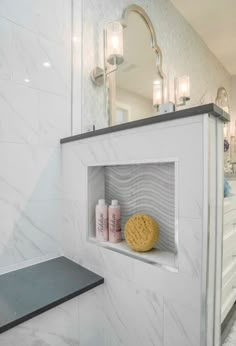 a bathroom with white marble walls and flooring, along with a shelf that holds various bath products