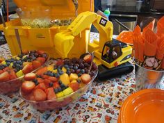 a table topped with bowls filled with fruit next to orange plates and utensils