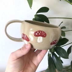 a hand holding a coffee cup with red mushrooms painted on the outside and white dots on the inside