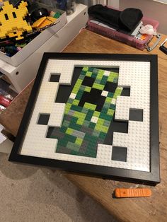 a framed piece of art made out of legos on a table next to other items