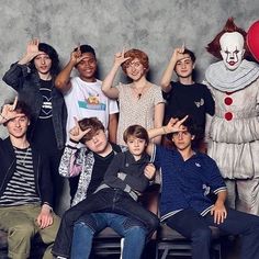 a group of people standing next to each other in front of a wall with a clown on it