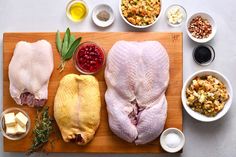 raw chicken on cutting board surrounded by ingredients for stuffing and sauces, including cranberry sauce