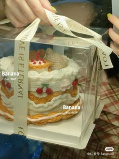 a person holding a cake in a clear box with ribbon around the top and bottom