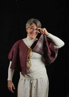 an older woman wearing glasses and a red cape smiles while standing in front of a black background