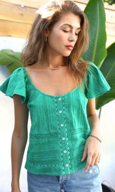 In an emerald shade, this relaxed top features a button front, lace detailing, and flutter sleeves. The lace decorations creates texture and dimension. The neckline lays in a unique way for an abstract silhouette. Flutter sleeve top Elastic sleeves Lace inserts Button front Self: 100% Cotton Length: 21 3/4" Chest: 18" Hand wash in cold water. Lay flat to dry. Low iron. Model is wearing a size small Style #: G234T6809 Green Casual Flutter Sleeve Top, Casual Green Top With Flutter Sleeves, Bohemian Green Tops With Ruffles, Summer Ruffle Sleeve Tops With Buttons, Green Flutter Sleeve Blouse For Summer, Bohemian Green Blouse With Buttons, Bohemian Green Tops With Buttons, Green Bohemian Blouse With Buttons, Green Casual Blouse With Lace Top