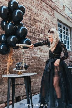 a woman in a black dress is holding some balloons