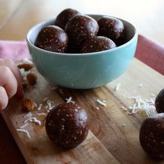 a child reaching for some food on a cutting board next to a bowl full of nuts