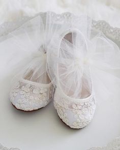 two pairs of white baby shoes on a lace doily with a tulle bow