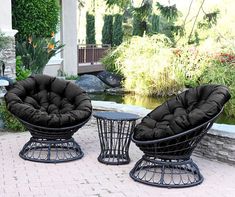 two black chairs sitting next to each other on a brick patio near a small pond