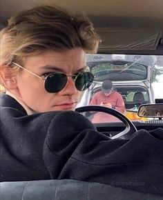 a woman wearing sunglasses driving a car with another man in the background