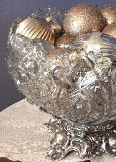 a glass bowl filled with silver ornaments on top of a tablecloth covered table cloth