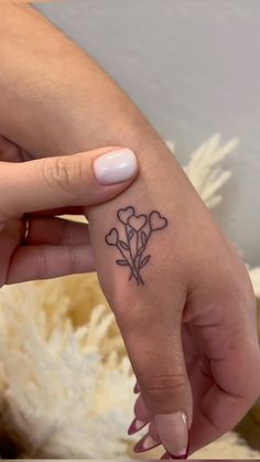 a woman's left hand with a small tattoo on the middle finger that has hearts and flowers