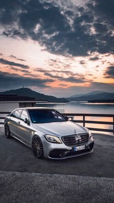 a silver car parked on top of a parking lot next to the ocean at sunset