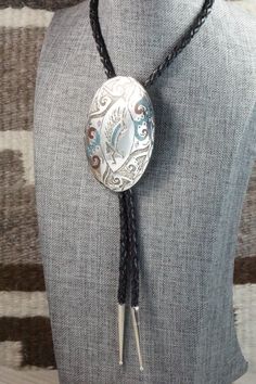 This turquoise & coral chip inlay, and sterling silver bolo tie features an eagle and was made by Navajo silversmith Raymond Begay. The back of the bolo tie is signed Ray B and stamped sterling.Tie Length: 23"Length: 3"Width: 2 1/8"Tips:Length: 1 5/8"Width: 1/4"Free shipping on all orders! We ship with USPS and always include tracking. All orders ship within a day of payment.Returns are accepted up to 30 days after you receive your order. Just send us a message. Our shop offers cash back or stor Western Style Oval Engraved Jewelry, Western Oval Engraved Jewelry, Traditional Adjustable Jewelry For Rodeo, Artisan Lariat Jewelry For Rodeo, Western Style Concho Jewelry For Shows, Western Style Engraved Jewelry For Rodeo, Western Engraved Jewelry For Rodeo, Engraved Silver Jewelry For Rodeo, Hand Tooled Western Silver Jewelry