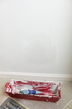 a red tray with a toothbrush in it next to a white wall and tools