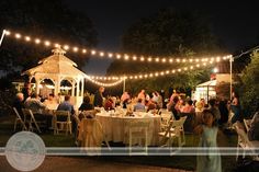 a group of people sitting around a table under string lights in a garden at night