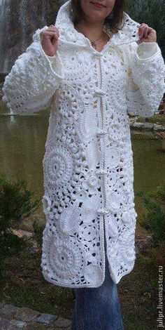 a woman wearing a white crochet jacket standing in front of a waterfall with her hands on her hips