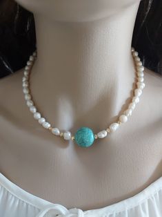 a woman wearing a necklace with pearls and a turquoise stone