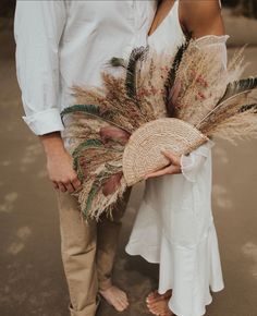 a man and woman standing next to each other holding hats with feathers on the sides