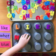 a child's hand is touching the letters in a muffin tin with magnets on it