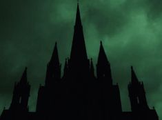 the silhouette of a gothic church against a dark green sky with clouds in the background