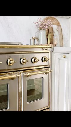 an old fashioned oven in a kitchen with white cabinets and gold trimmings on the doors