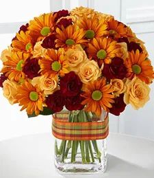 a vase filled with lots of orange and red flowers on top of a white table