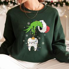 Spread Cheer with Our Christmas Dentist Sweatshirt - Funny Lights Tooth Crewneck for a Dental Squad Celebration! Celebrate the festive season with a dental twist! Our Christmas Dentist Sweatshirt is the perfect blend of humor and holiday spirit. Featuring the whimsical Funny Christmas Light Tooth Held by the Grinch's Hand, this sweatshirt is not just for dentists - it's for the entire Dental Squad ready to bring smiles to the season. Light up your Christmas with dental humor and order your festive shirt today. 'Tis the season to be jolly, and our dental squad shirts are here to make it extra merry and bright! 💥I. ABOUT PRODUCT - There are many ways to express your personality and wearing our products with eye-catching patterns and meaningful words is one of the ways. Comfortable, casual, Christmas Green Sweatshirt With Graphic Print, Green Long Sleeve Tops As Gift, Christmas Green Graphic Print Sweatshirt, Funny Christmas Lights, Christmas Dental, Dental Assistant Gifts, Grinch Hands, Dragon Ball Z Shirt, Assistant Gifts