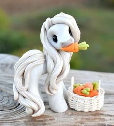 a white pony figurine sitting on top of a wooden table next to a basket of carrots