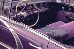 the interior of an old fashioned car with purple cloth and leather seats, including steering wheel