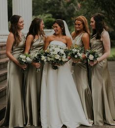 a group of women standing next to each other in front of a white building holding bouquets