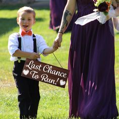 a young boy holding the hand of an adult in a purple dress and bow tie