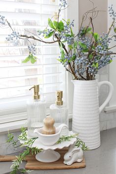 a vase with blue flowers in it sitting on a counter next to two candles and soap dispensers