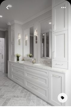 a large bathroom with white cabinets and marble counter tops, along with two vases filled with flowers