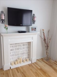 a flat screen tv mounted above a fireplace with candles on the mantel below it