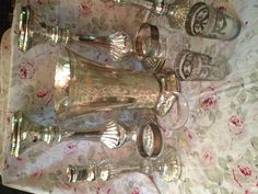 a table topped with lots of silver vases and glasses on top of a table cloth