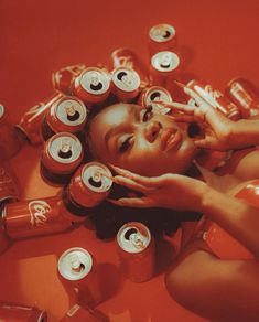 a woman laying on the ground surrounded by cans of sodas and orange juice, with her hands in her face