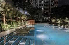 an empty swimming pool with lounge chairs and palm trees in the foreground at night