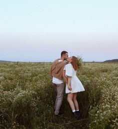 a man and woman kissing in the middle of a field with wildflowers at sunset